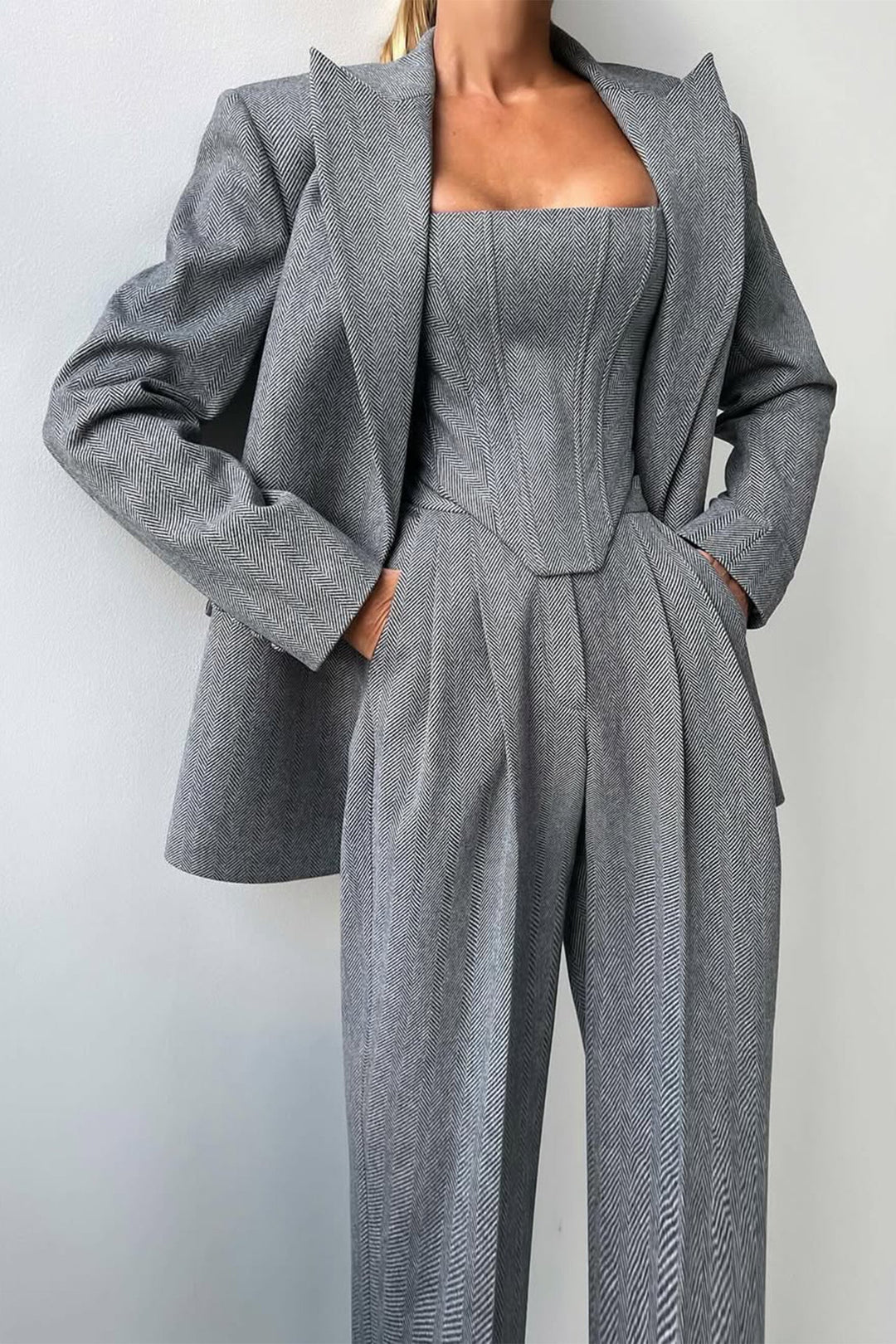 A woman wearing a double-breasted blazer with a matching top and trousers, all in a gray color.